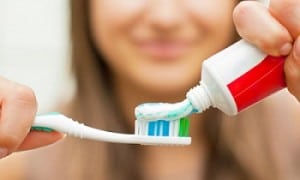 Mulher desfocada colocando creme dental na escova de dentes